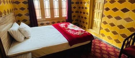 Una habitación con cama, una silla, ventilador de techo y ventana con cortinas.