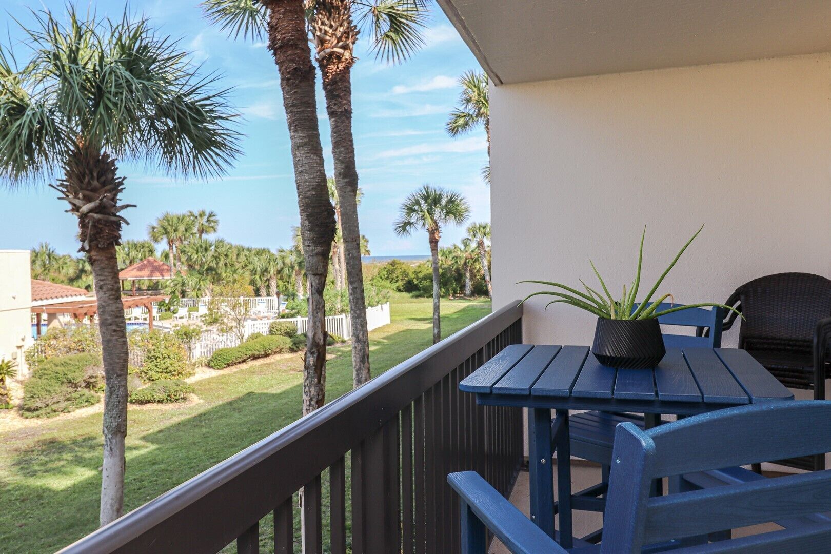A balcony with a table and chairs, overlooking a well-maintained lawn and palm trees.