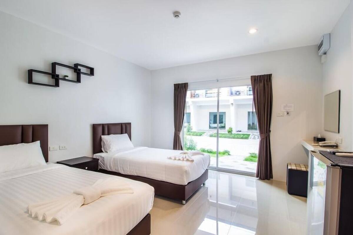 A hotel room with two beds, a desk, and a view of the outside.