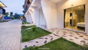 A modern hotel exterior with a paved walkway, a grassy area, and a glass door entrance.