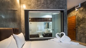 A hotel room with a large bed, a wooden door, and a shower area visible through a glass door.
