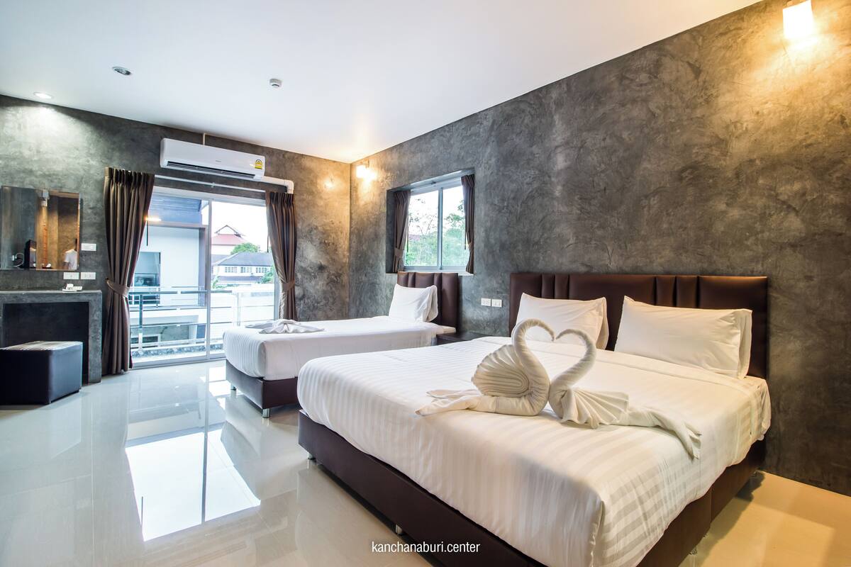 A modern hotel room with two beds, a large window, and a view of the outside.