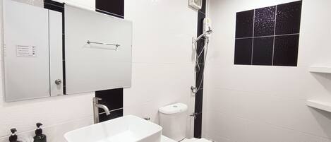 Un baño con lavamanos blanco, inodoro, ducha y espejo.