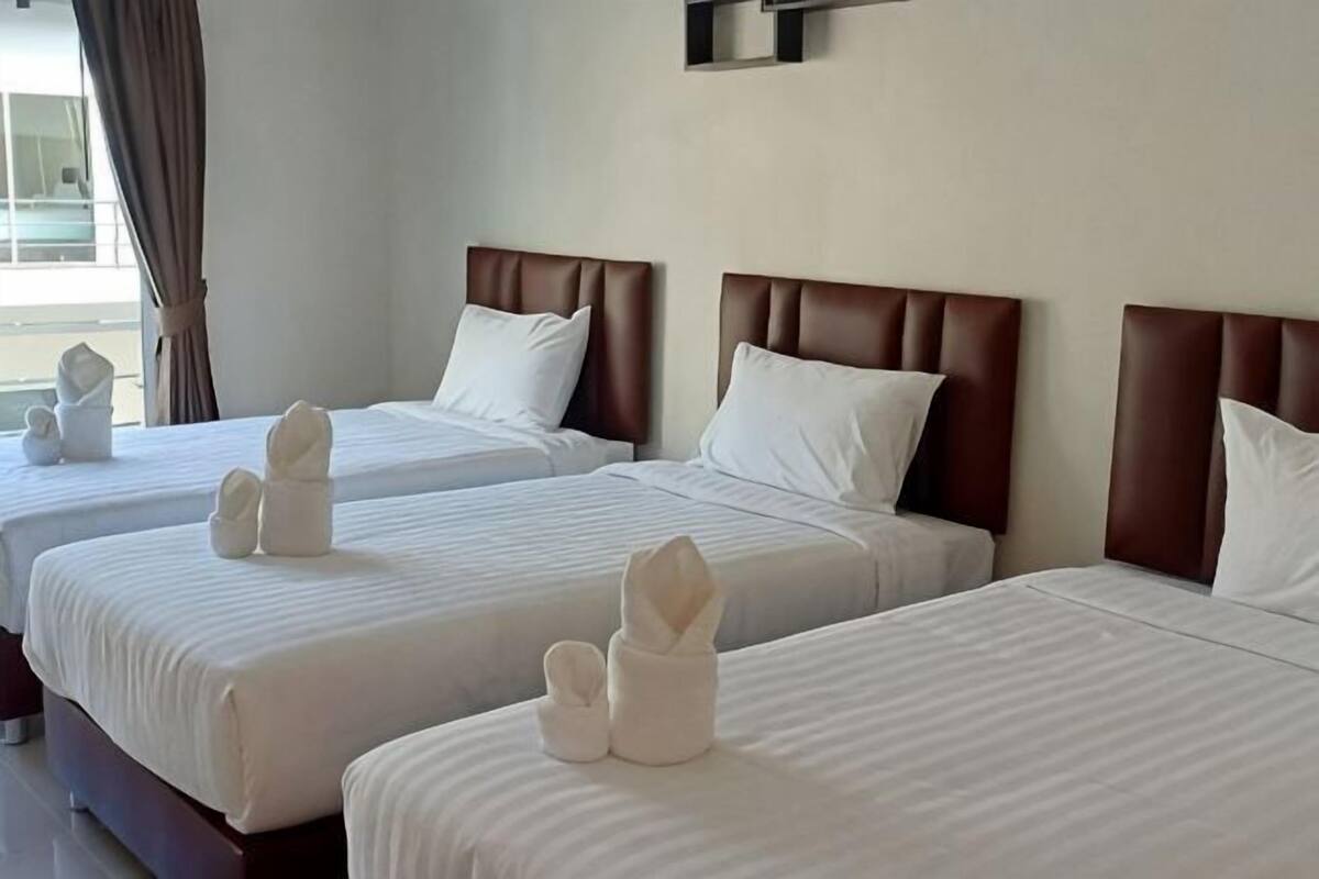 A hotel room with three beds, each with a brown headboard and white bedding.