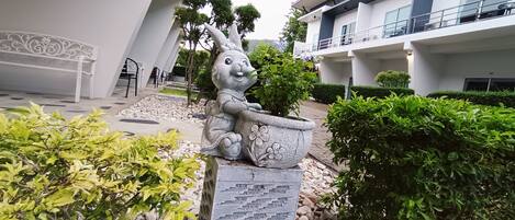 A modern building with a statue of a rabbit holding a flower pot, surrounded by greenery and a stone pathway.