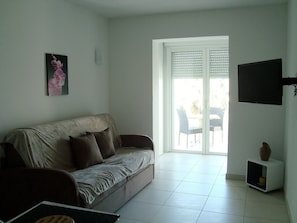 A living room with a sofa, a TV, and a small table with a vase. - Studio N°2 in Tiuccia, waterfront, air-conditioned, wifi (Tiuccia)