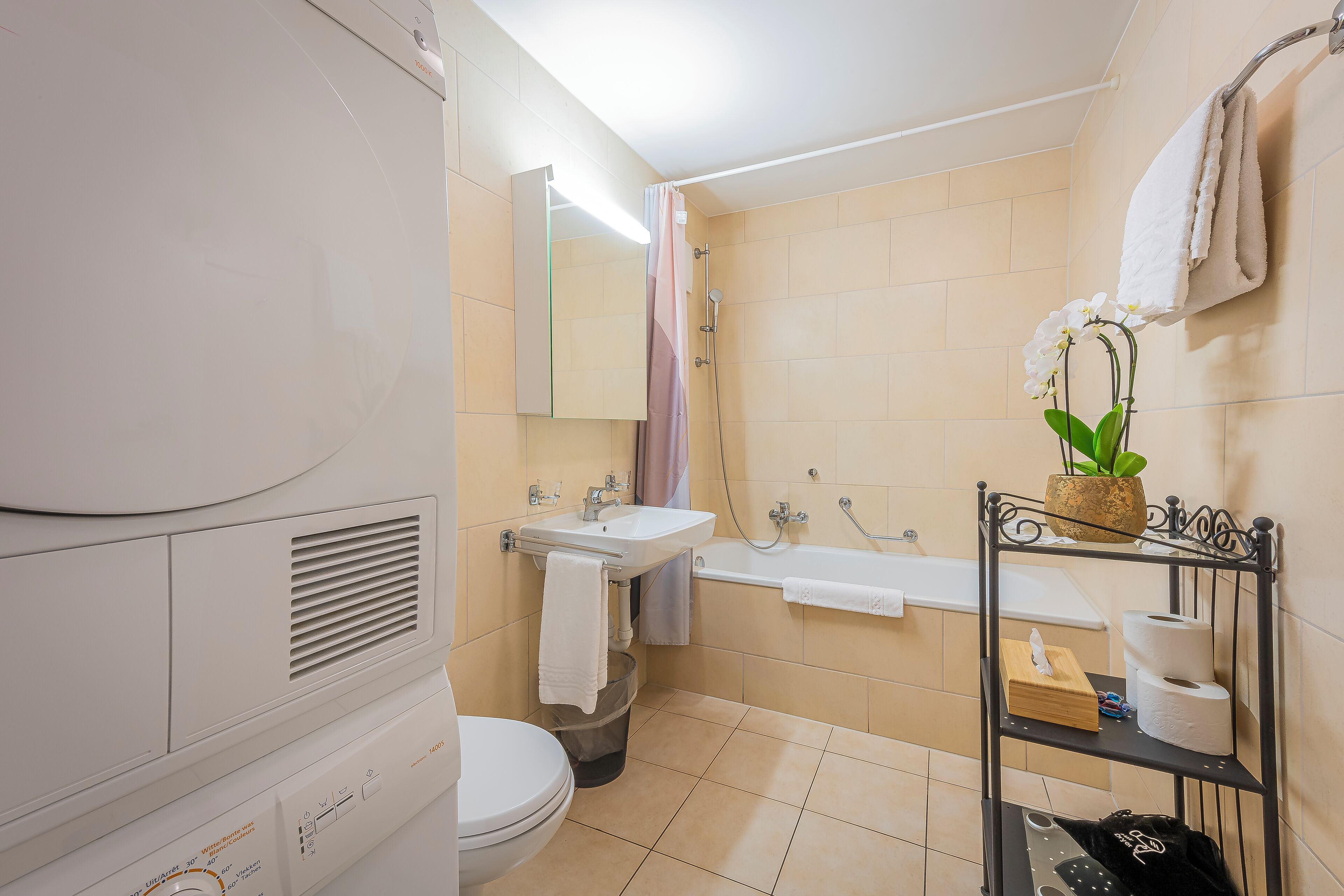 Un baño con inodoro, lavamanos, ducha y estante con toallas y artículos de aseo.