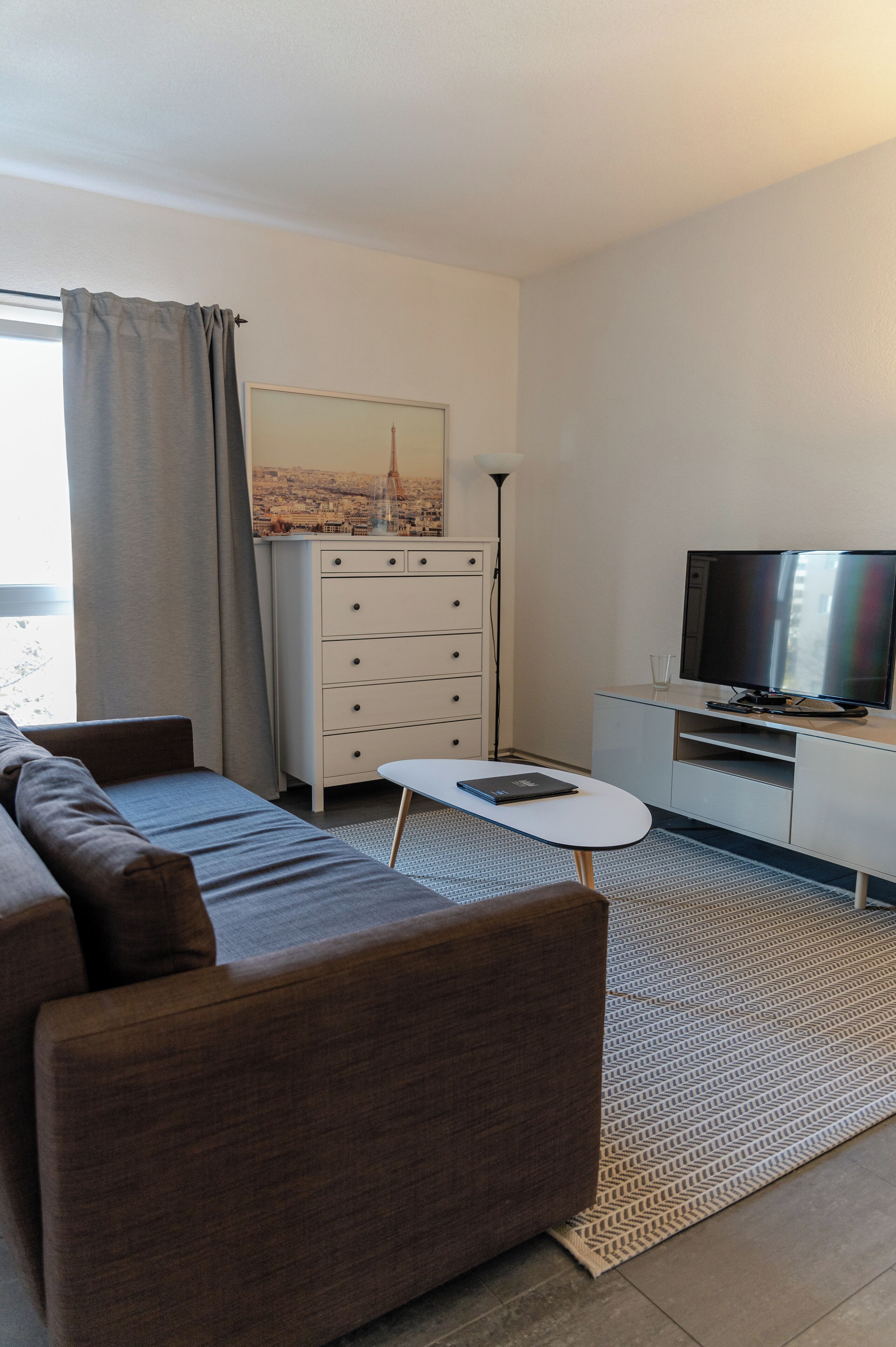 Een moderne woonkamer met een bank, een kleine tafel, een televisie en een dressoir.