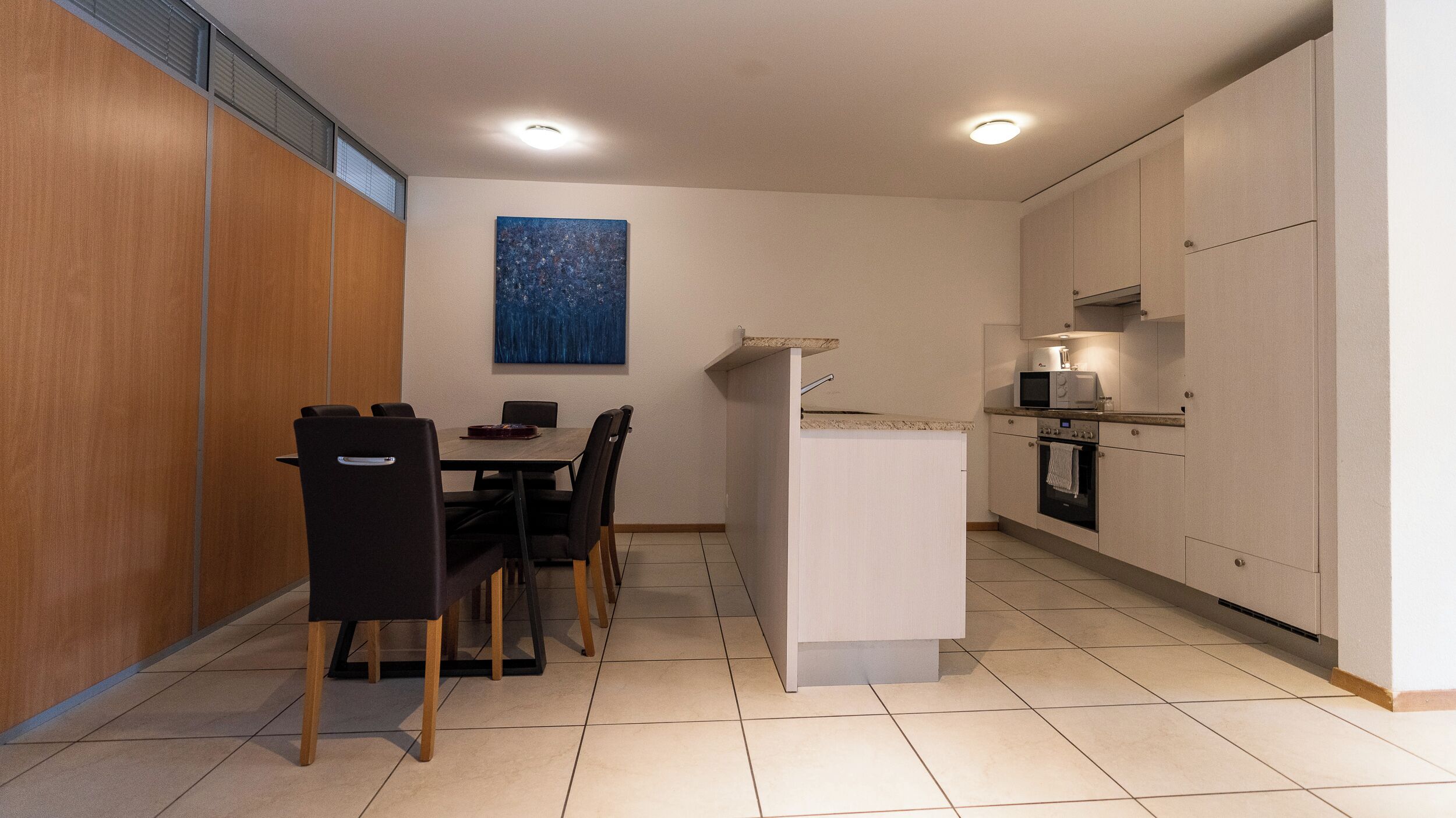 A compact kitchen with a dining area, a microwave, an oven, and a painting on the wall.