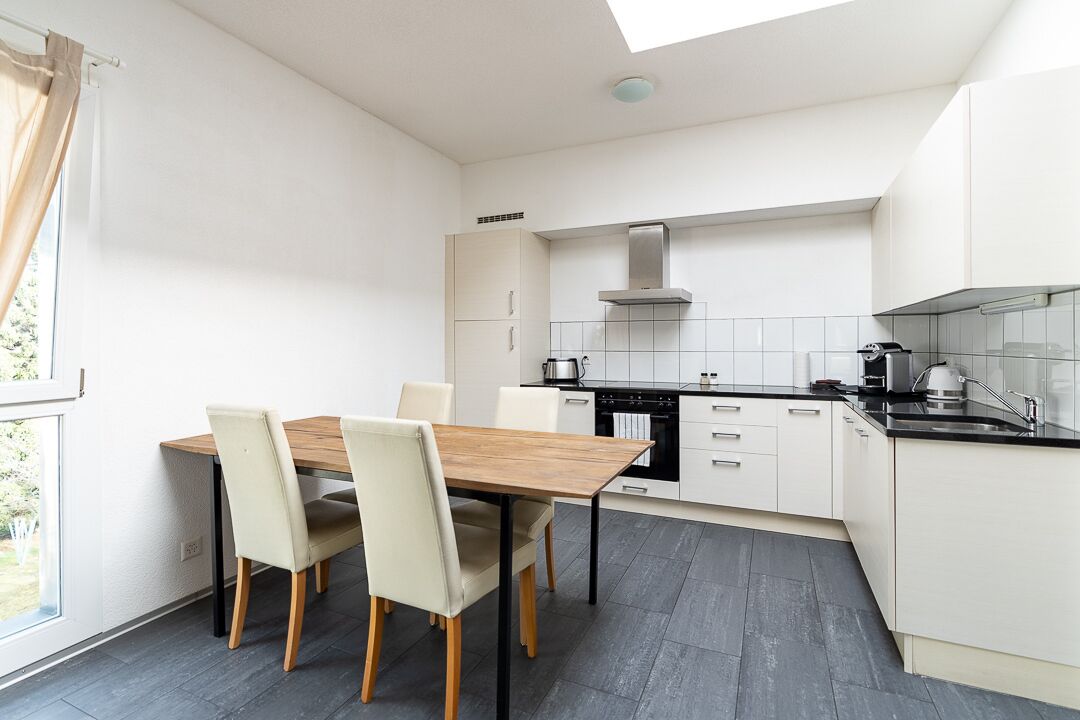 A modern kitchen with white cabinetry, a black countertop, and a wooden dining table with four chairs.