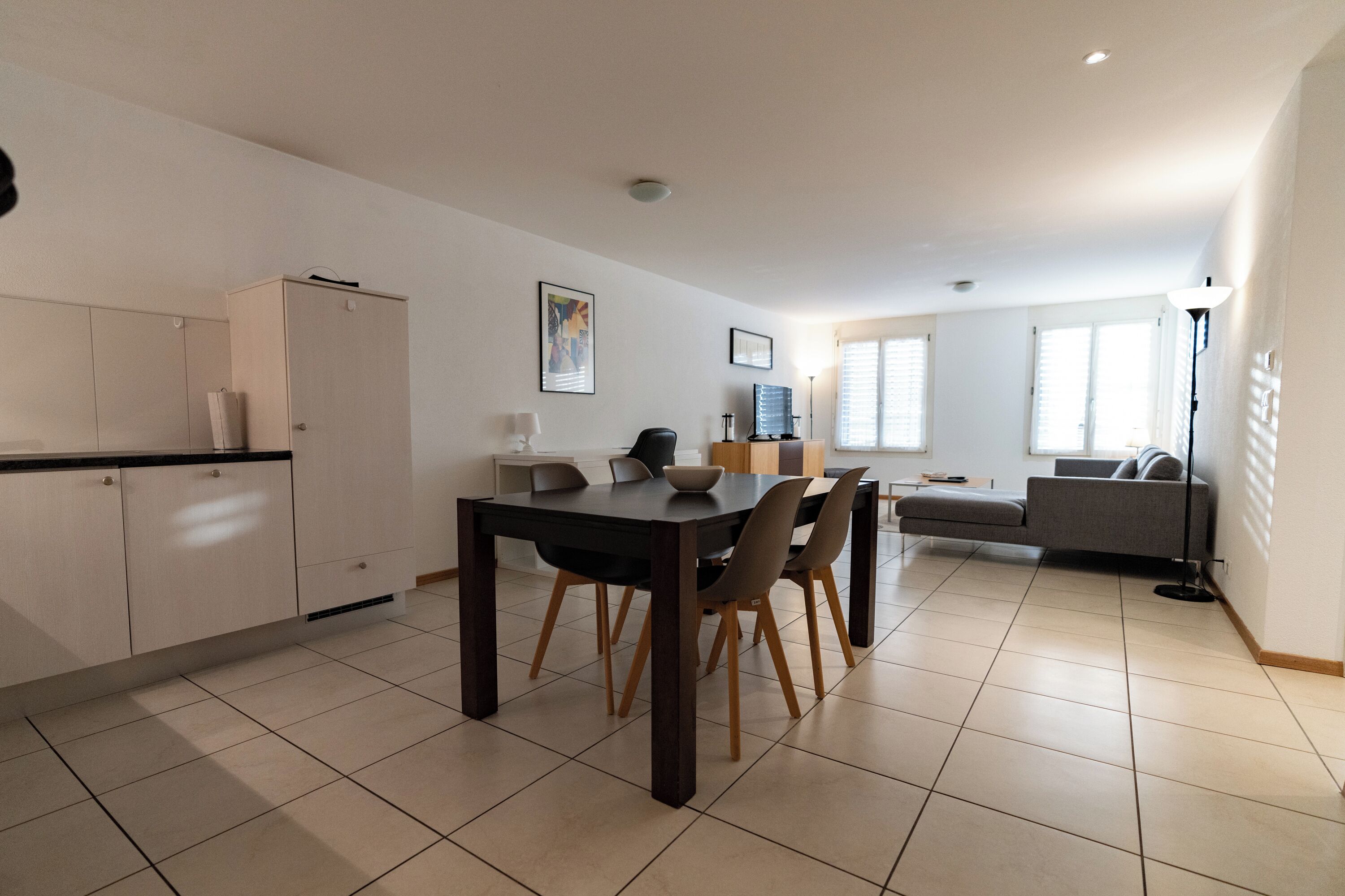 A modern kitchen with a dining table, chairs, and a sofa in the living area.