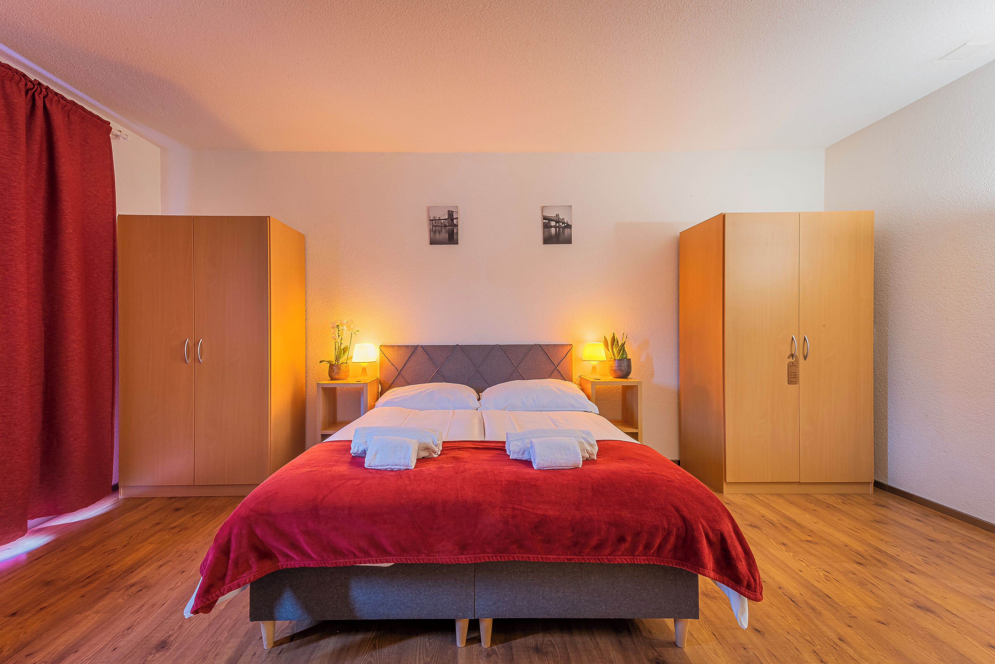 Ein ordentlich bezogenes Bett mit roter Decke, zwei Nachttischlampen und Holzschränken.