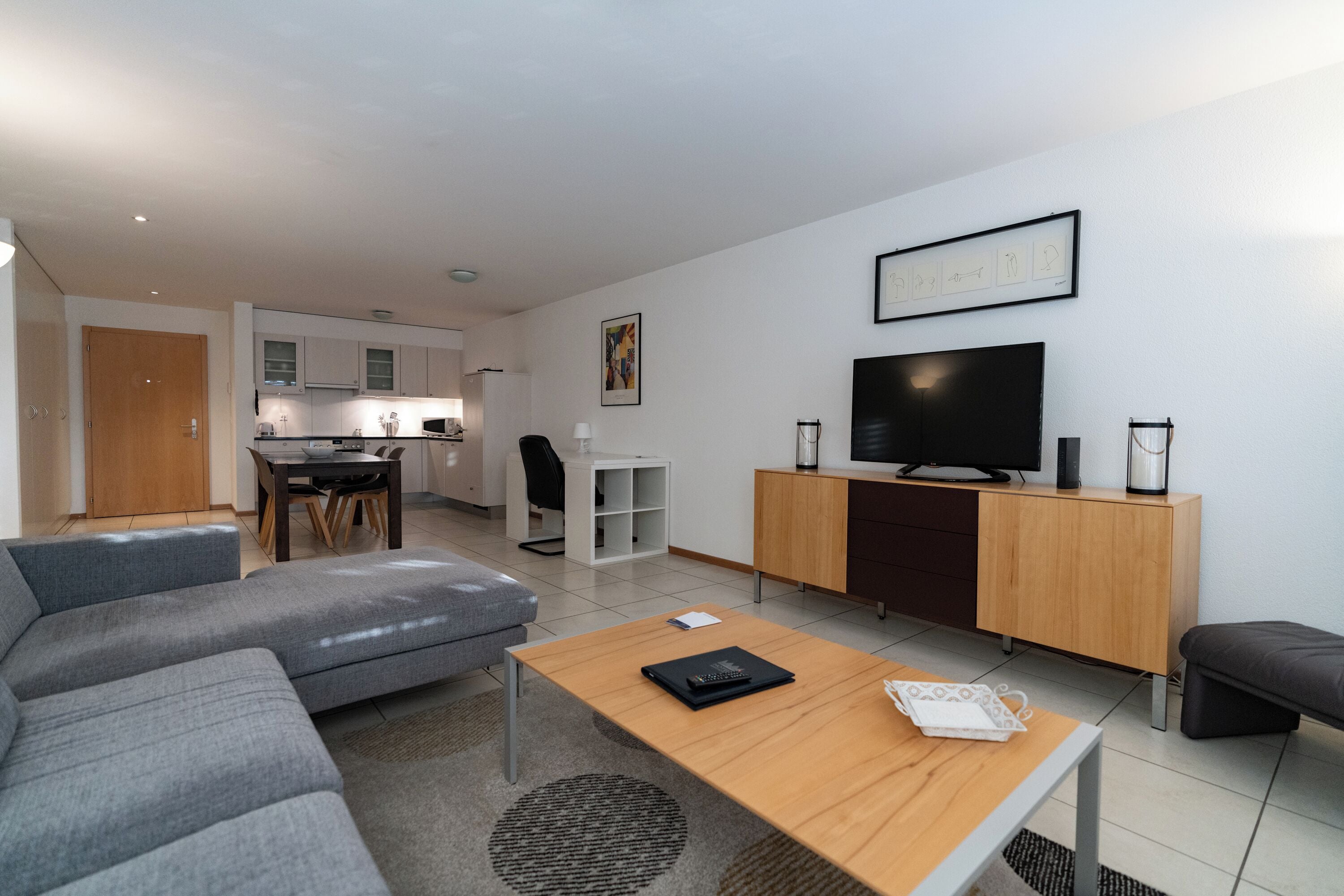 Un salon moderne avec un canapé gris, une table basse en bois et un téléviseur posé sur un meuble en bois.
