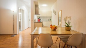 A modern kitchen with white cabinets, a wooden dining table, and a vase of flowers. - Los Lorentes Residences - Bulle (Bulle)