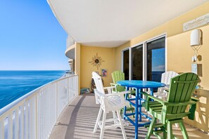 A balcony with a view of the ocean, featuring a table and chairs, a sun decoration, and a welcome sign.