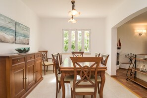A dining area with a wooden table and chairs, a cabinet with drawers, a window with a view of greenery, and a ceiling light fixture.