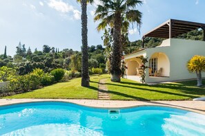 A swimming pool with a clear blue water, surrounded by a well-maintained lawn and palm trees. - Villa Bandicoot, Lagoa de Momprolé, Algarve (Loulé)