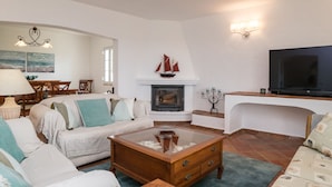A living room with a fireplace, a television, and a dining area with a table and chairs. - Bandicoot Villa, Lagoa de Momprolé, Algarve (Loulé)