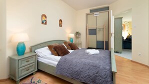 A bedroom with a bed, nightstands, a lamp, a door, and a hallway leading to another room.