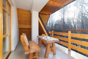 Un balcón de madera con una mesa y bancos, con vistas a un área boscosa.
