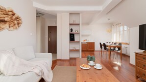 A modern living room with a white sofa, wooden dining table, and a kitchen area with cabinets and a refrigerator. - Stylish Apartment in Zakopane | Balcony | Close to Krupówki Street (Zakopane)