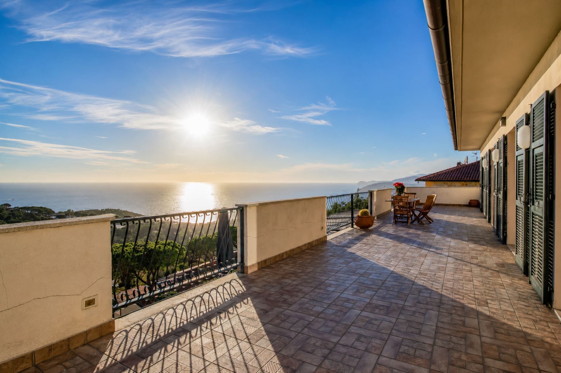 A balcony with a view of the sea, a table with chairs, and a potted plant.