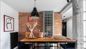 Un comedor con pared de ladrillo, una lámpara colgante, una mesa de madera y un florero con ramas decorativas.