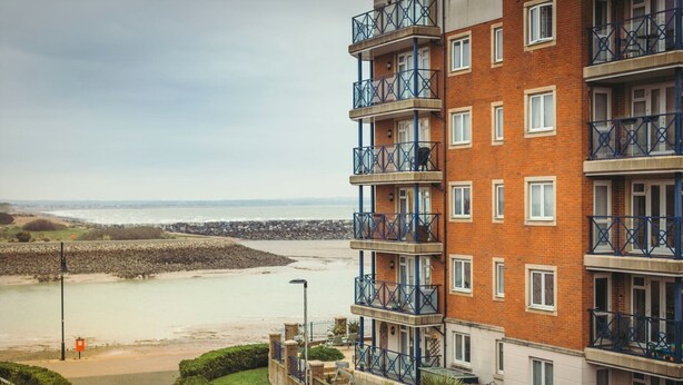 Un edificio residenziale a più piani con balconi, vista sulla spiaggia e un muro in pietra sullo sfondo.