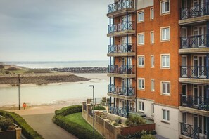 A multi-story residential building with balconies, a view of the beach, and a stone wall in the background. - Sovereign Sunrise near to beach (Eastbourne)