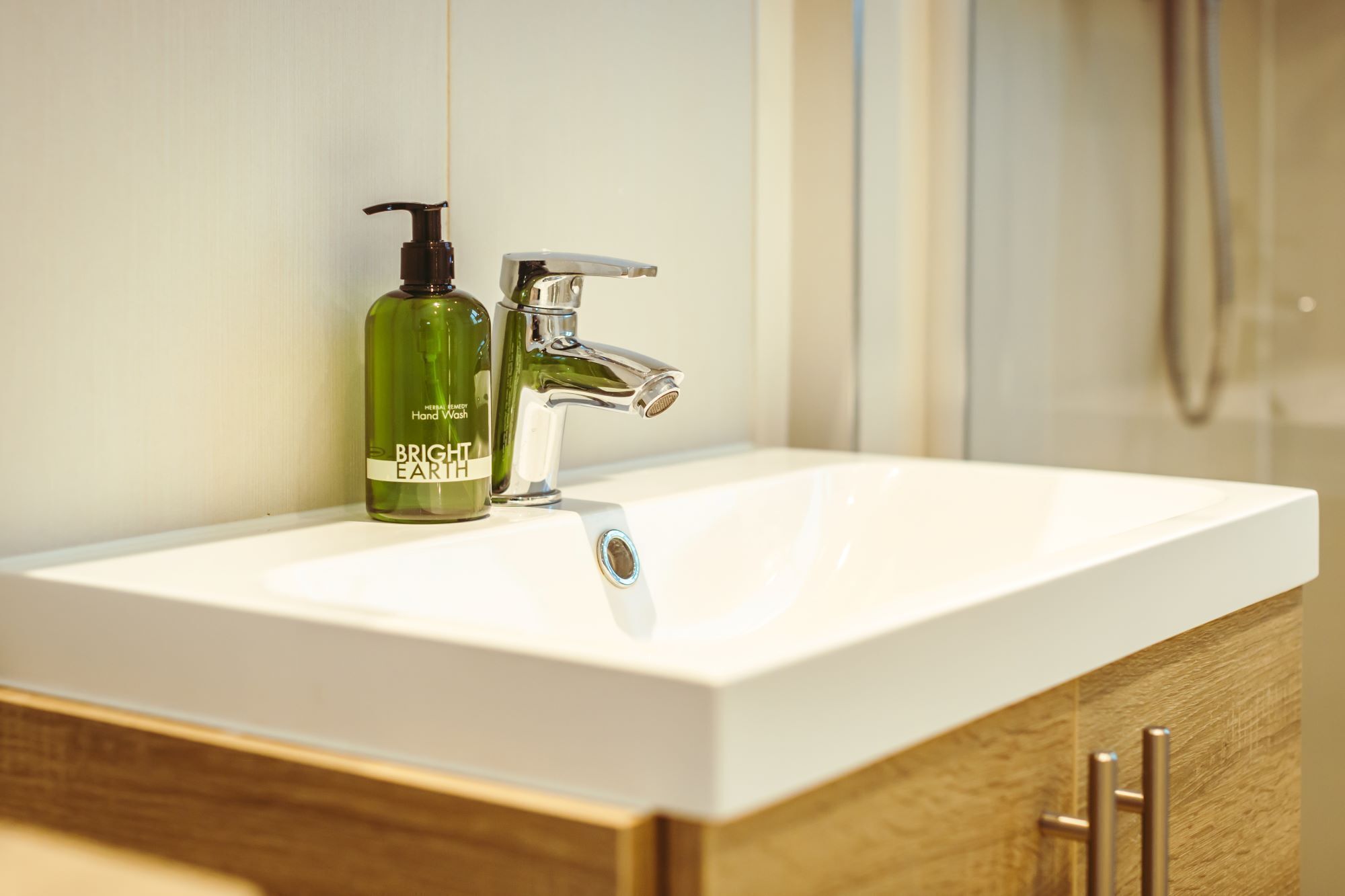 Un baño con un lavabo blanco, una botella verde de jabón Bright Earth y un grifo cromado.