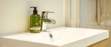 Un baño con un lavabo blanco, una botella verde de jabón Bright Earth y un grifo cromado.