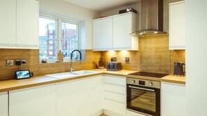 Una cucina moderna con mobili bianchi, una cappa in acciaio inossidabile, forno integrato e una finestra che offre vista sugli edifici circostanti.