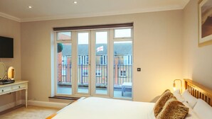 Una camera da letto con un letto grande, un comodino con una lampada, una finestra che si affaccia su una zona residenziale e una porta che dà su un balcone.