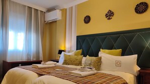 Une chambre d’hôtel avec un grand lit, deux tables de chevet, une petite table et un climatiseur fixé au mur.