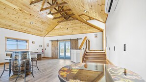 A spacious room with a high wooden ceiling, a large barrel table, and a staircase leading to another area.