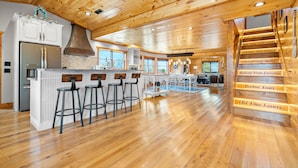 A spacious kitchen with wooden flooring, a central island with bar stools, and a staircase with decorative metal railings.