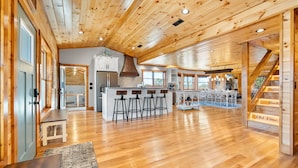 A spacious kitchen with wooden floors, a central island with stools, and a staircase with a metal railing.