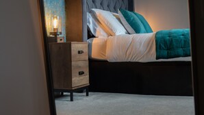 Un dormitorio con un cabecero capitonado, una mesita de noche con lámpara, y una cama con ropa de cama blanca y verde azulado.