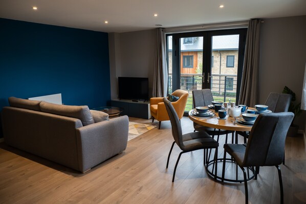 A modern living room with a sofa, a dining table set for four, and a TV.