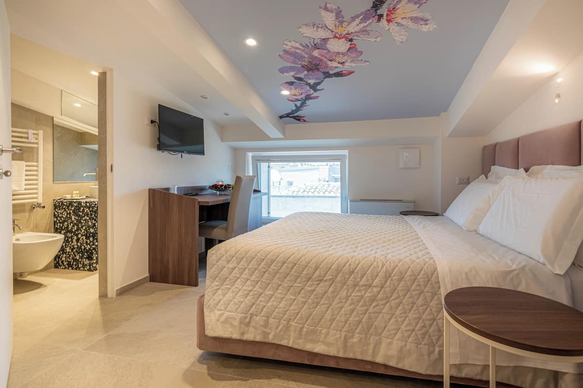 Quarto com cama grande, escrivaninha e televisão na parede.