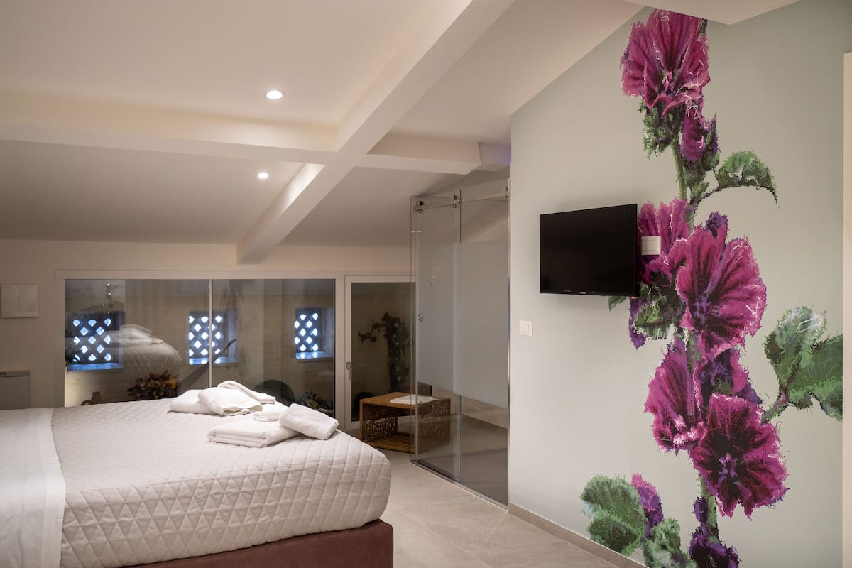 Quarto moderno com cama grande, box de vidro e televisão de tela plana na parede.