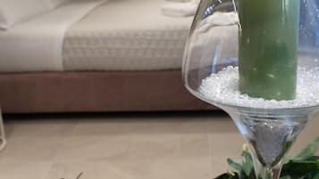 A room with a bed, a green candle in a glass holder, and a table with greenery.