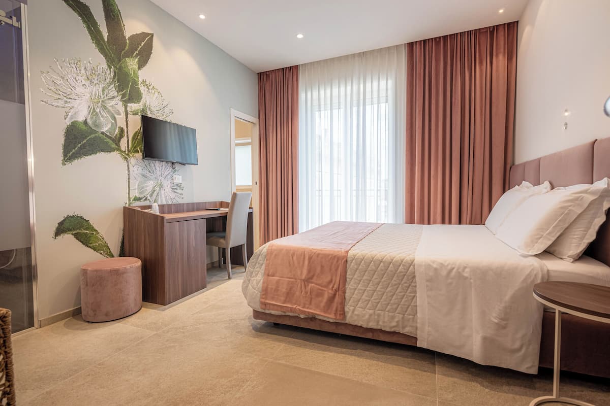 Quarto de hotel moderno com uma cama grande, uma escrivaninha, televisão e uma janela ampla com cortinas.
