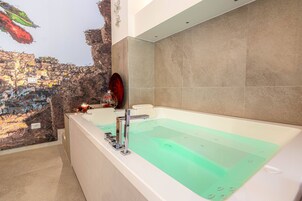 Un bagno moderno con una grande vasca, un muro in pietra e uno specchio decorativo.