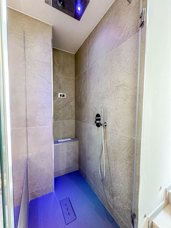 Une salle de bain moderne dotée d’une douche, d’un banc intégré et d’une prise électrique visible au sol.