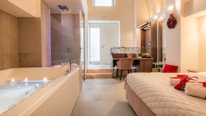 Une chambre d’hôtel moderne avec une grande baignoire, un lit avec des oreillers rouges, un bureau et une petite table sur laquelle est posé un vase de fleurs.