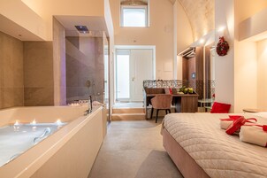 Una moderna camera d'albergo con una grande vasca da bagno, un letto con cuscini rossi, una scrivania e un piccolo tavolino con un vaso di fiori.