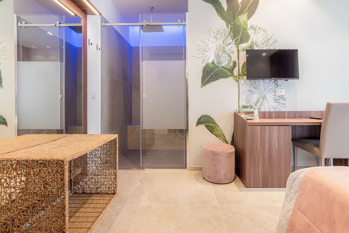 Une chambre d’hôtel moderne avec une porte d’entrée en verre, un bureau en bois, une télévision et une plante en pot.