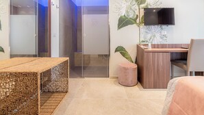 Une chambre d’hôtel moderne avec une porte d’entrée en verre, un bureau en bois, une télévision et une plante en pot.