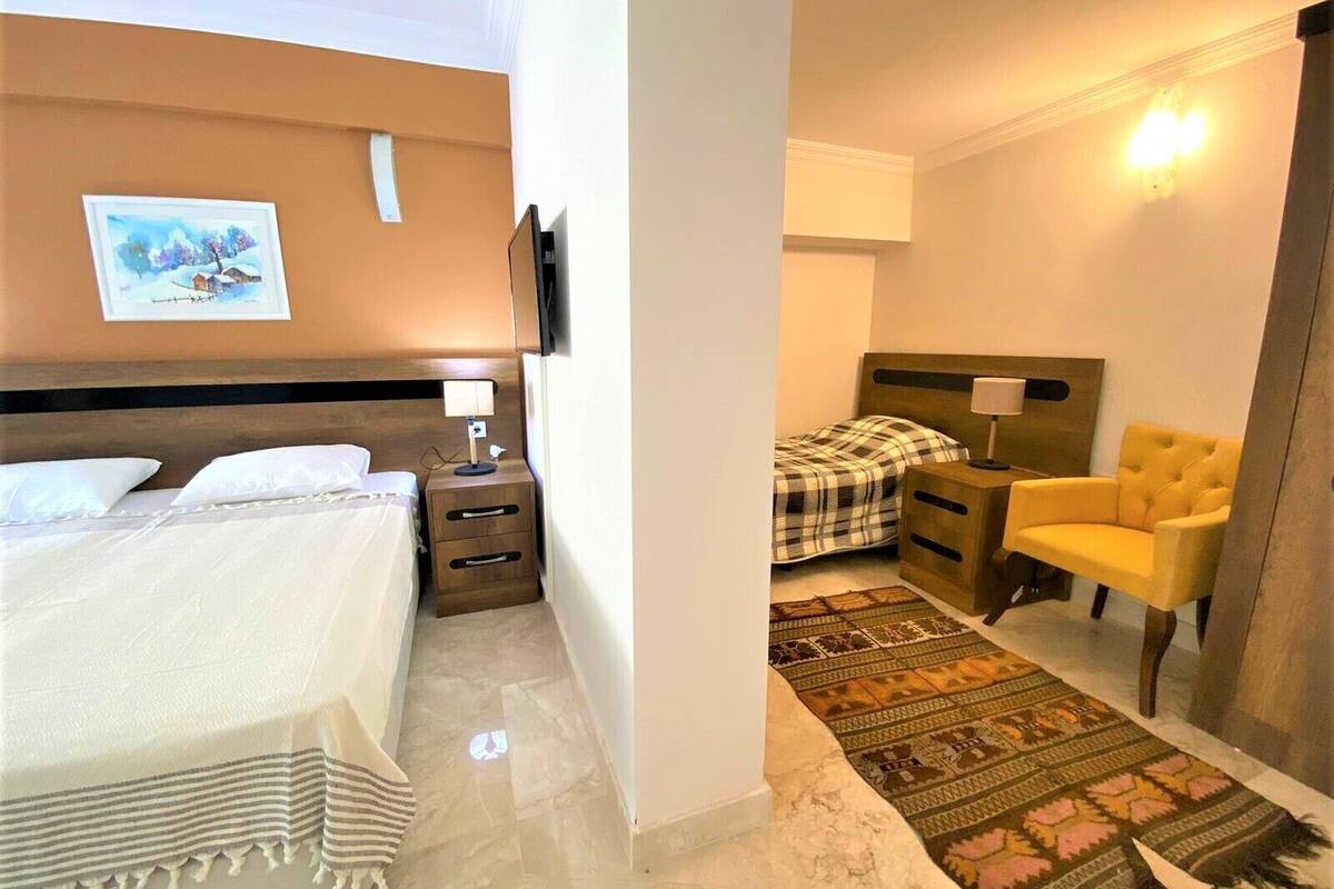 Una camera d'albergo con un letto, un comodino, una sedia, un tappeto e un quadro appeso al muro.